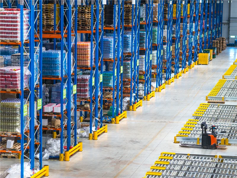 Warehouse aisle with tall blue metal racking filled with pallets and goods in storage